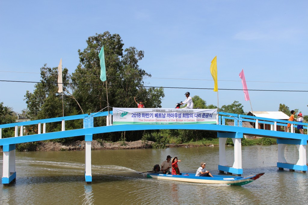 완공된 '희망의 다리'를 건너는 주민들과 배로 강을 지나는 주민들